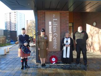 Four individuals standing alongside a poppy wreath in front of the Lilias Centre